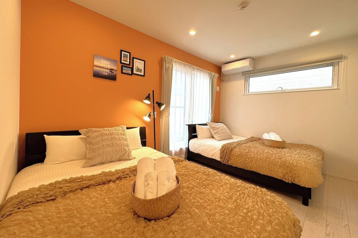A hotel room with two beds, a large window with curtains, an air conditioning unit, and a wall with framed pictures.