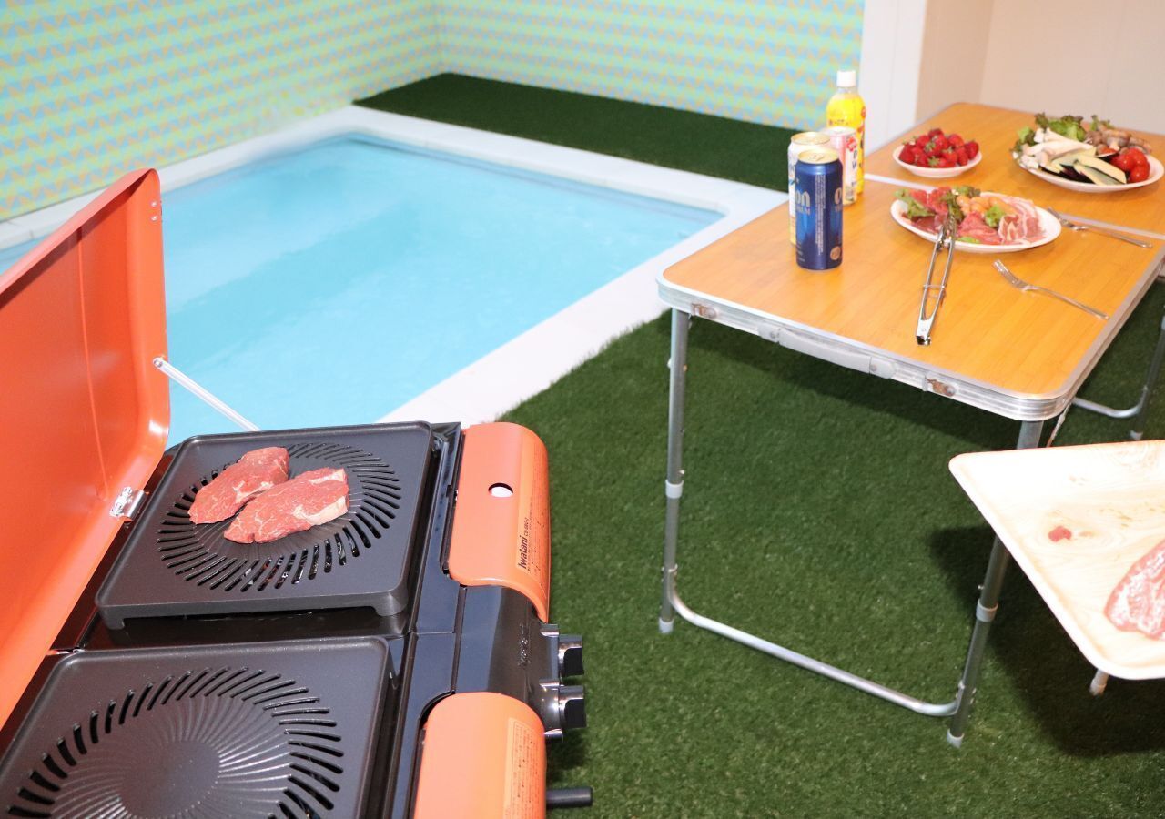Een zwembadterras met een barbecue en een tafel met eten en drinken.
