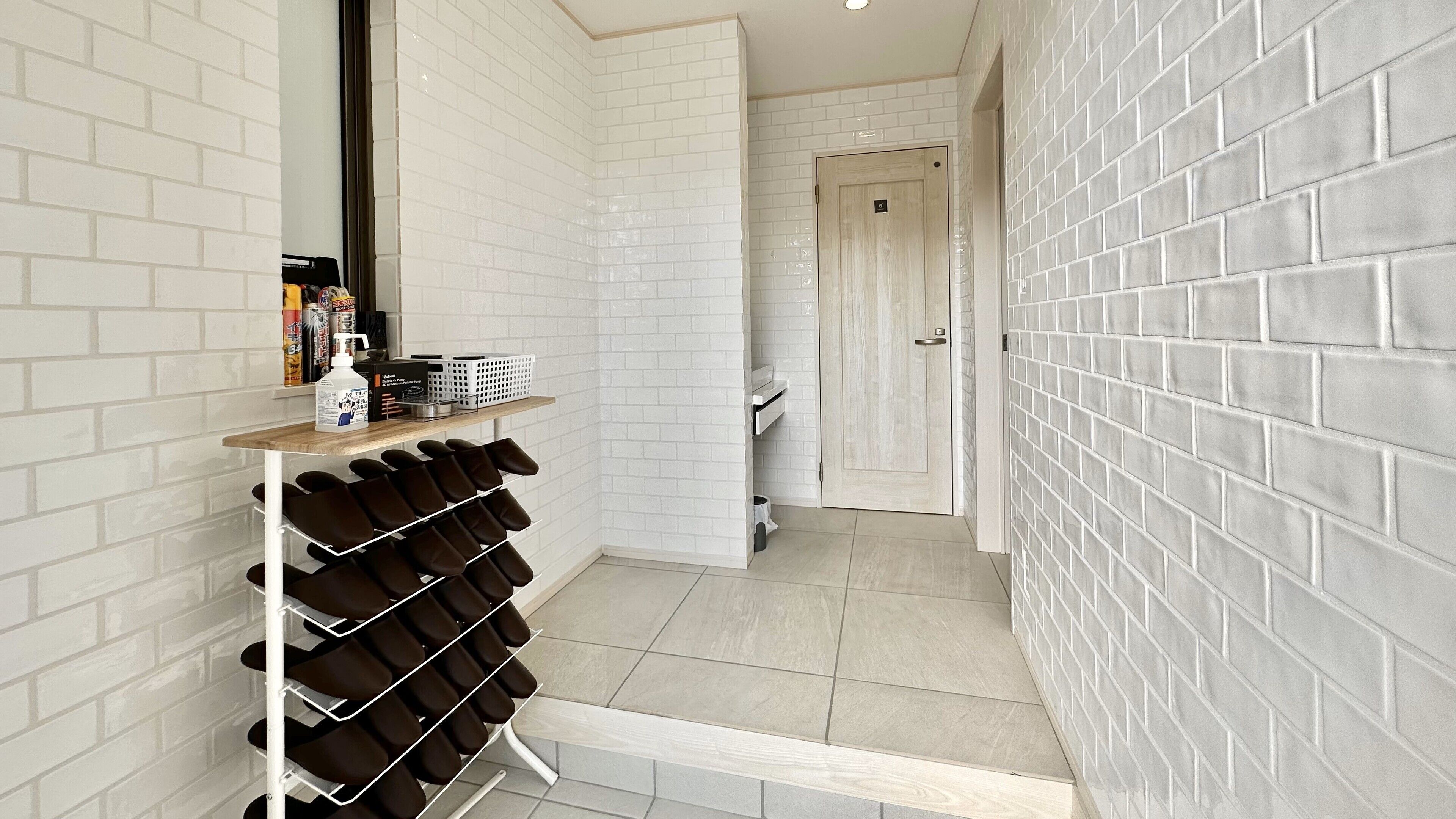 A hallway with white brick walls, a shoe rack, and a door leading to another room.