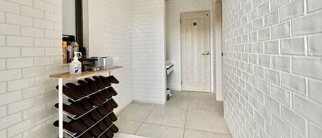 A hallway with white brick walls, a shoe rack, and a door leading to another room.