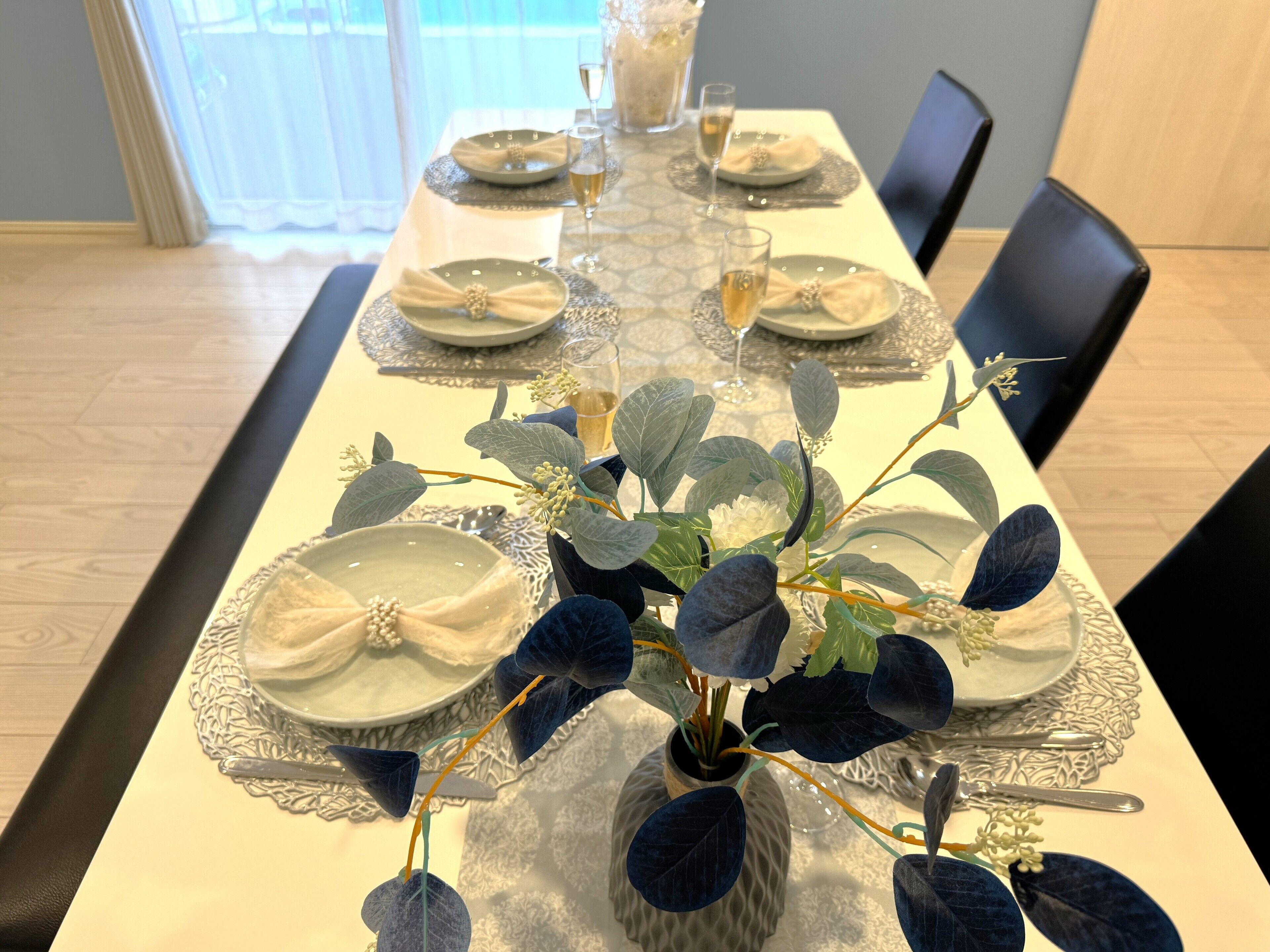 Une table à manger dressée avec des assiettes, des verres et un centre de table composé de feuillages.