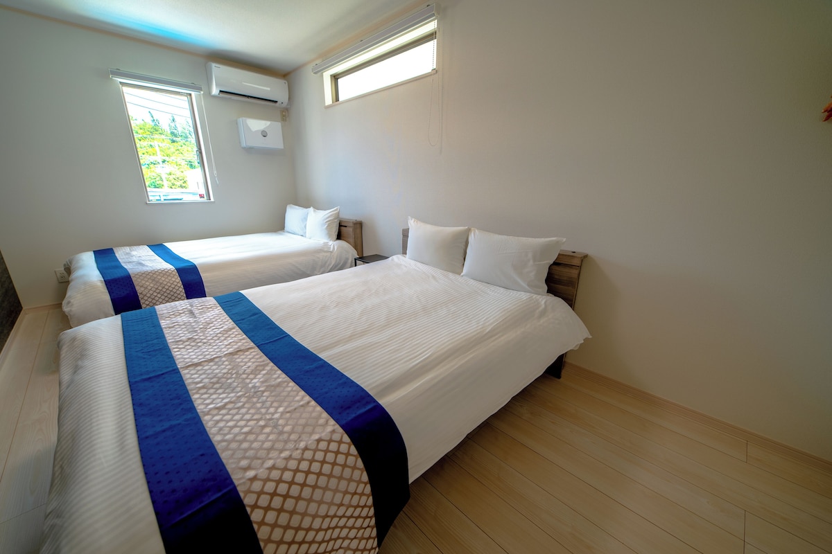 A hotel room with two beds, each with a blue and white bedspread, and a window providing natural light.