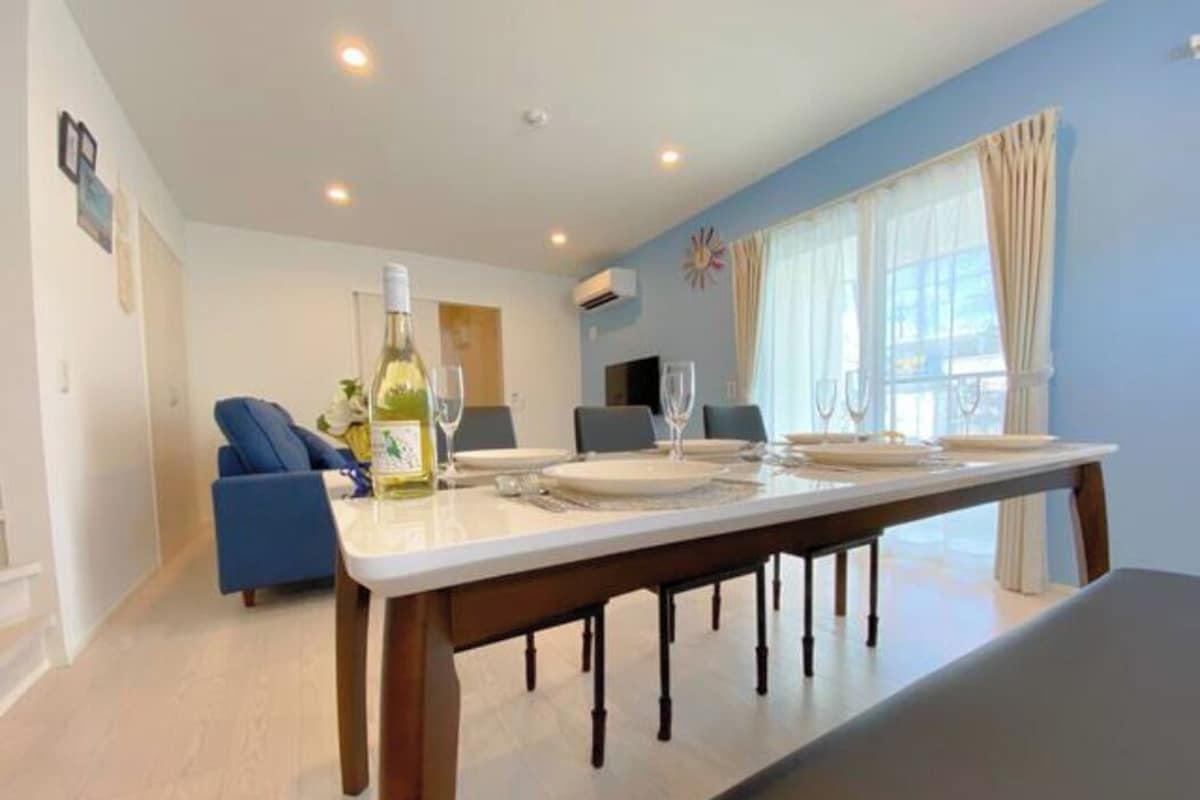 A dining area with a long table set for six, a bottle of wine, and a blue sofa in the background.