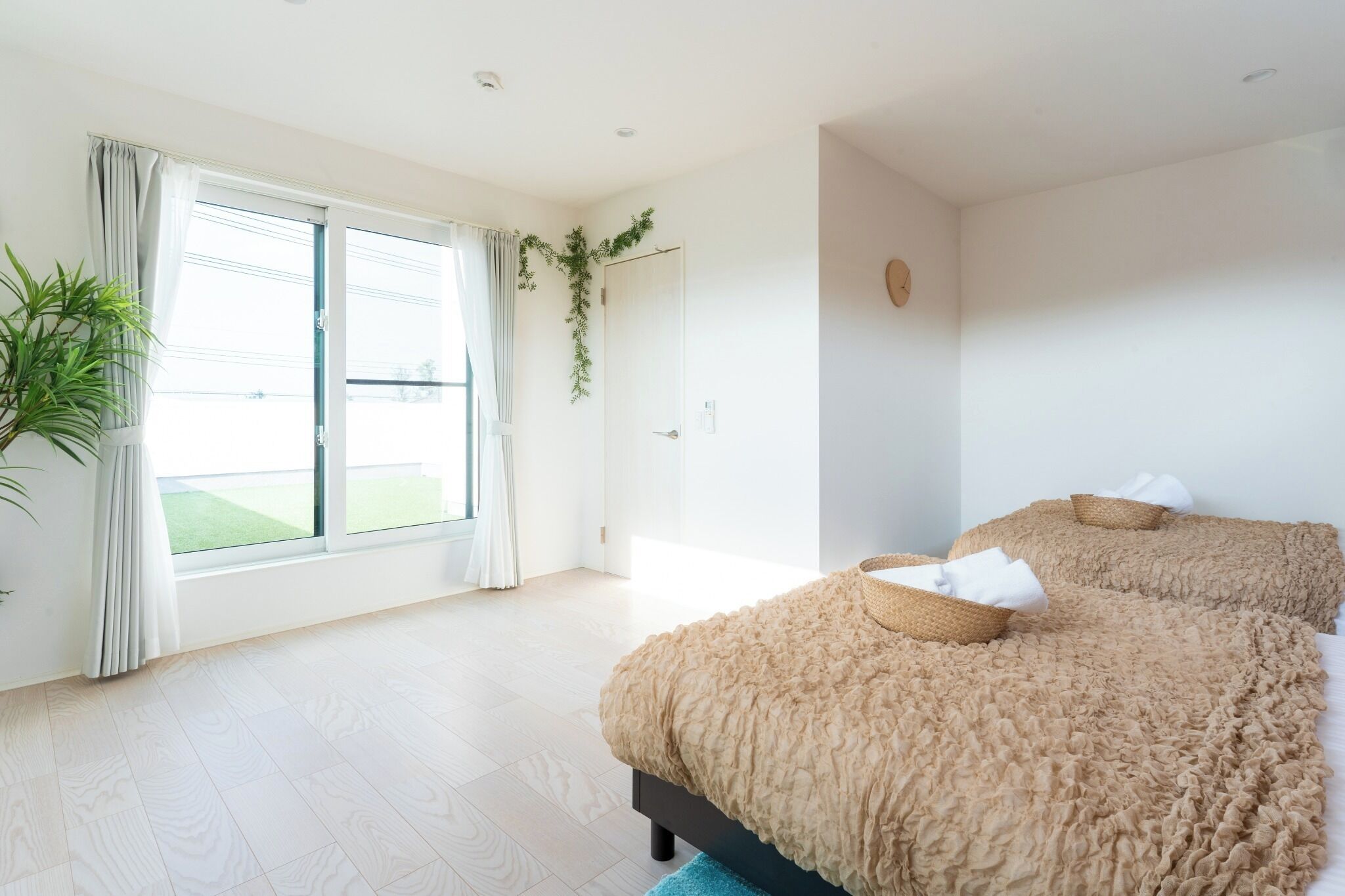 Een slaapkamer met een groot raam, een bed met een gevlinderd beddegoed en een potplant.
