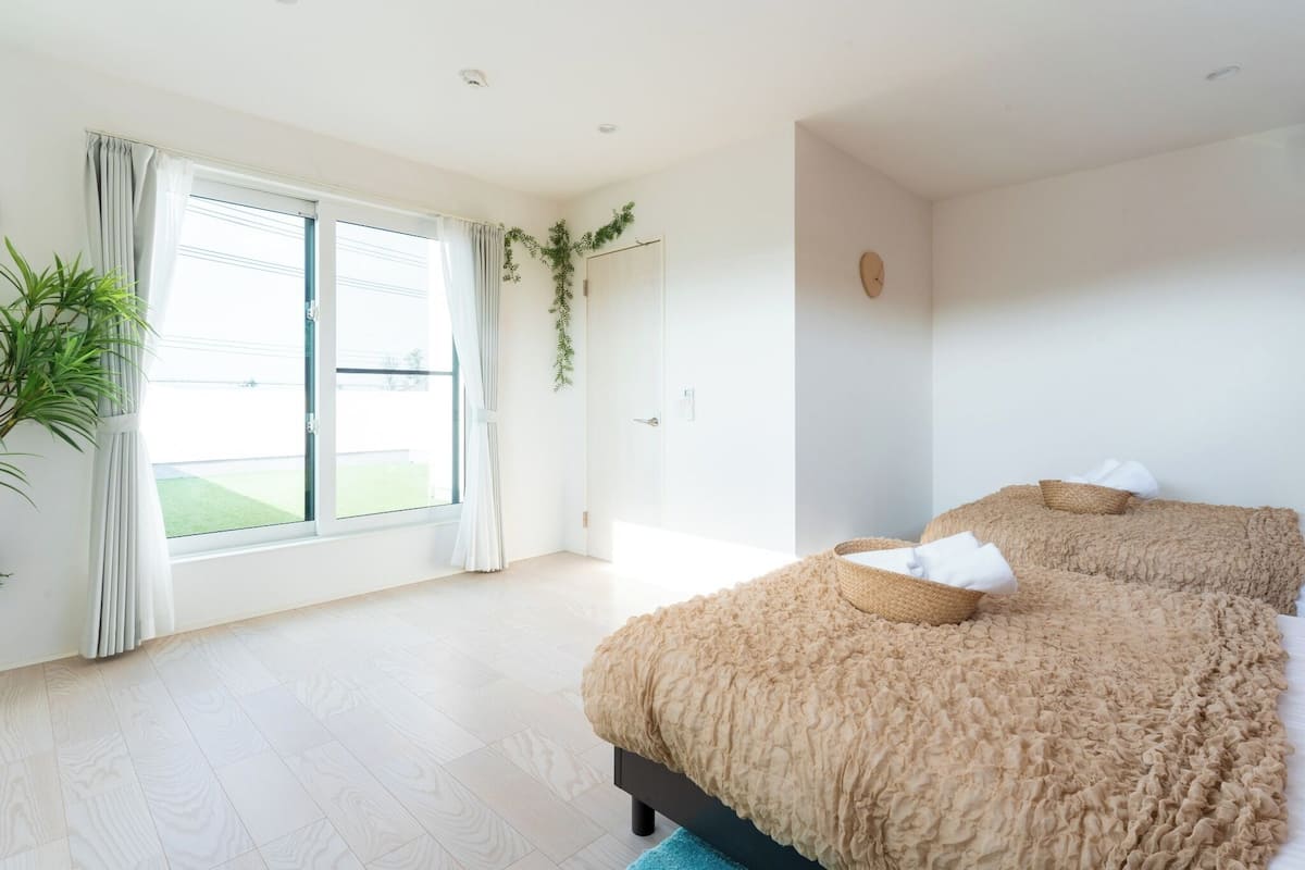 A bedroom with a large window, a bed with a ruffled cover, and a potted plant.