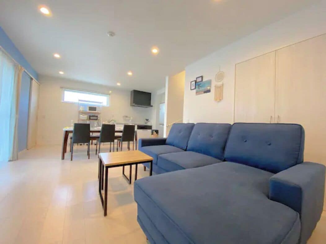 A modern living room with a blue sofa, a wooden coffee table, and a dining area with chairs and a table.