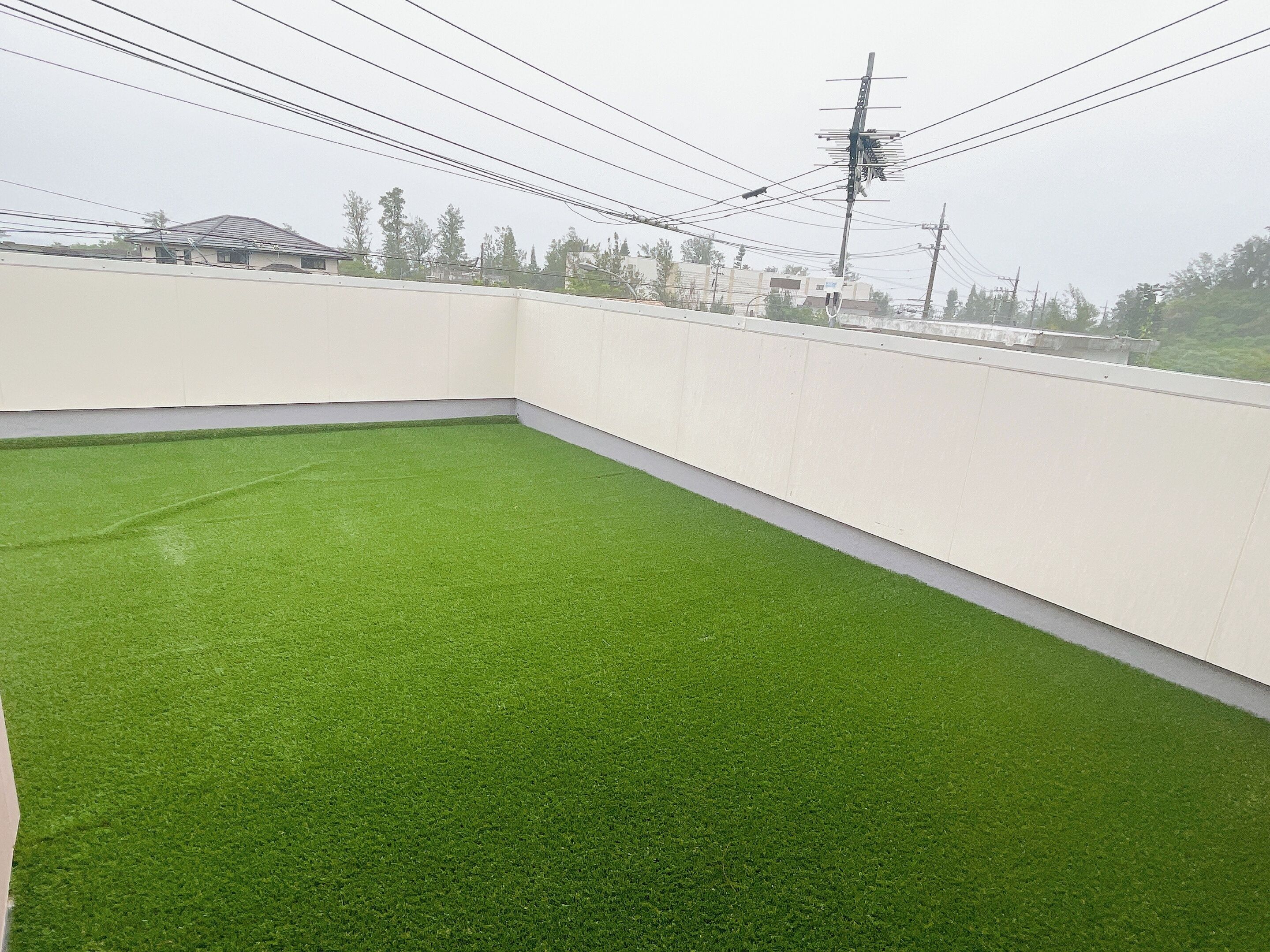 Un toit-terrasse recouvert d’un gazon synthétique, avec des murs blancs et des lignes électriques.