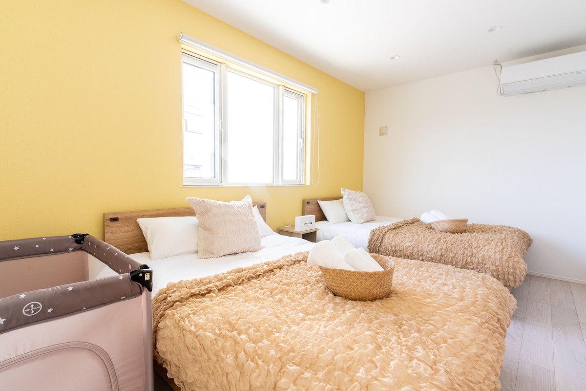 A hotel room with two beds, a window, and a crib.