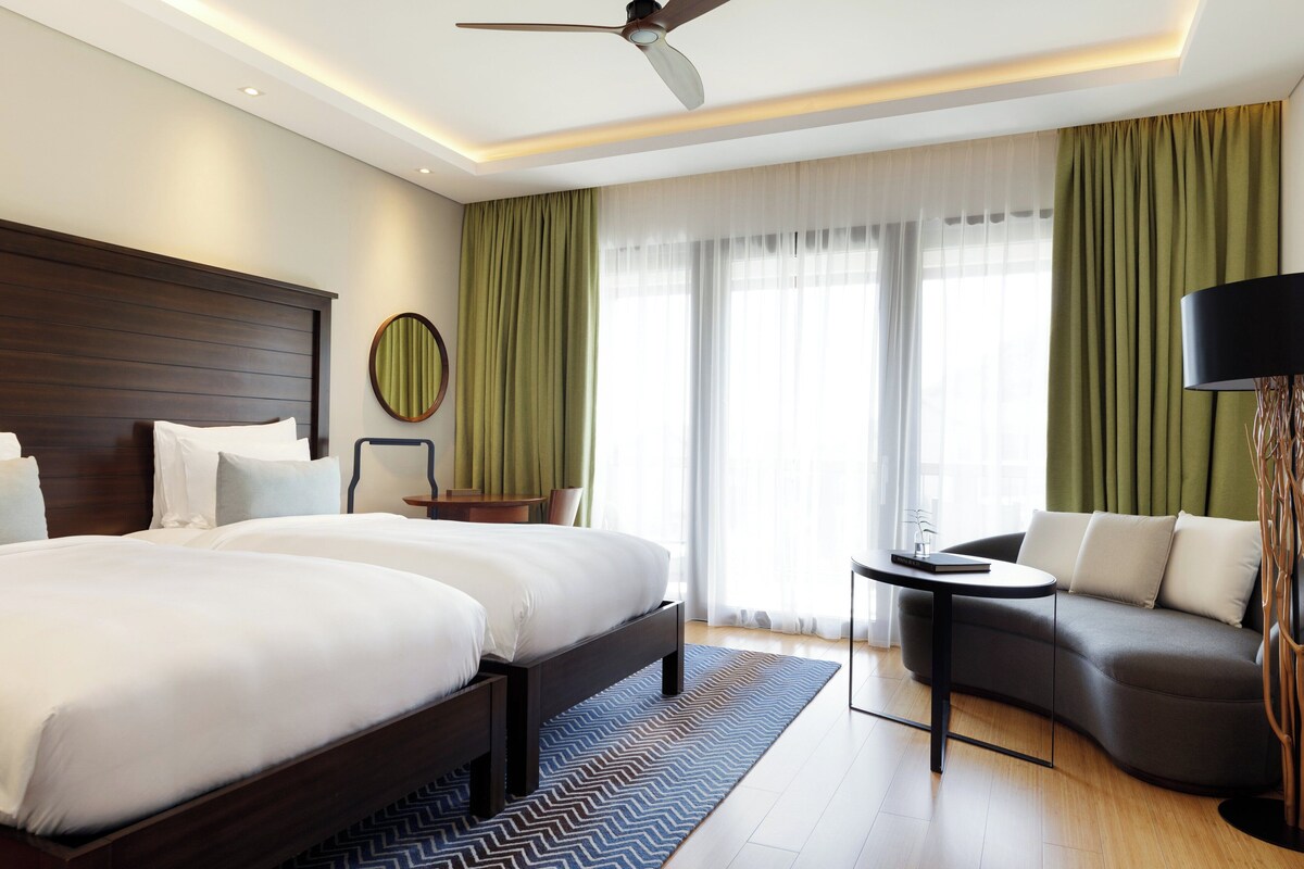 Una habitación de hotel moderna con una cama grande, un sofá, una mesita y un ventilador de techo.