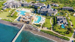 Eine Vogelperspektive eines Resorts mit mehreren Gebäuden, einem großen Swimmingpool und einem Strandbereich.