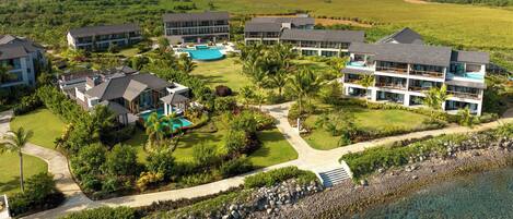 A resort with multiple buildings, a swimming pool, and a view of the sea and mountains.