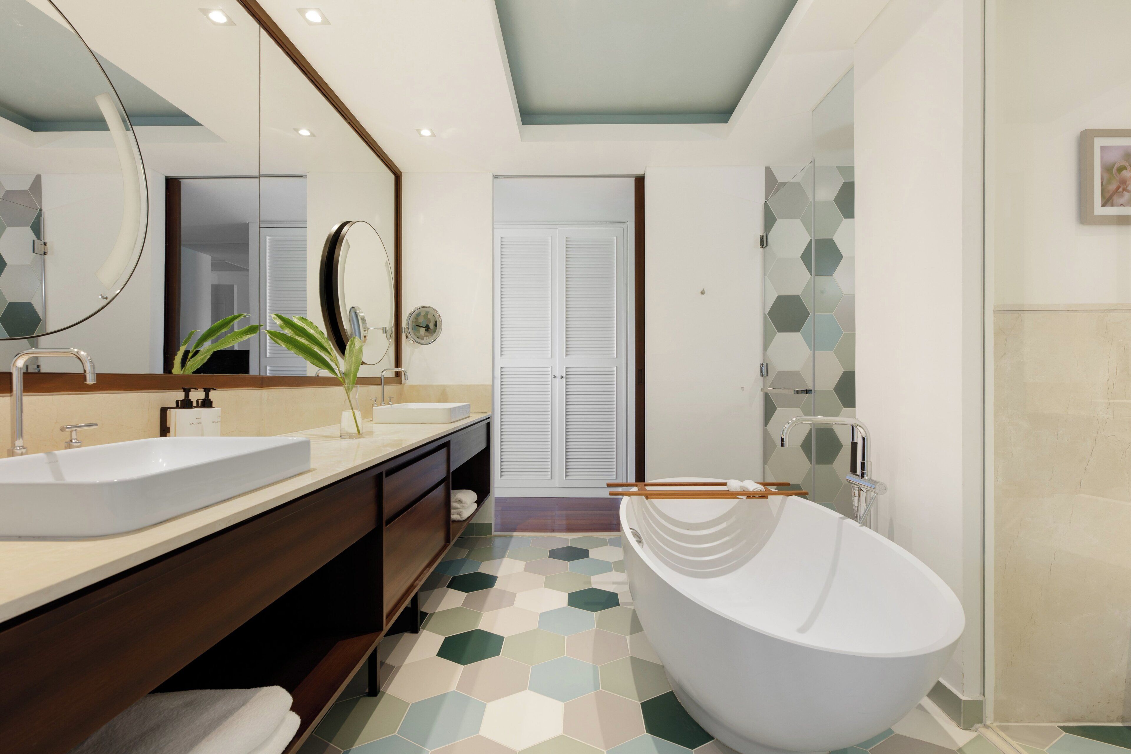 A modern bathroom with a freestanding bathtub, two sinks, and a large mirror.