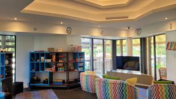 A living room with a large TV, colorful bean bag chairs, and a bookshelf filled with toys and books.