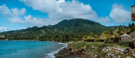 A beach with a mountain in the background, a clear sky, and a structure with stairs on the right.