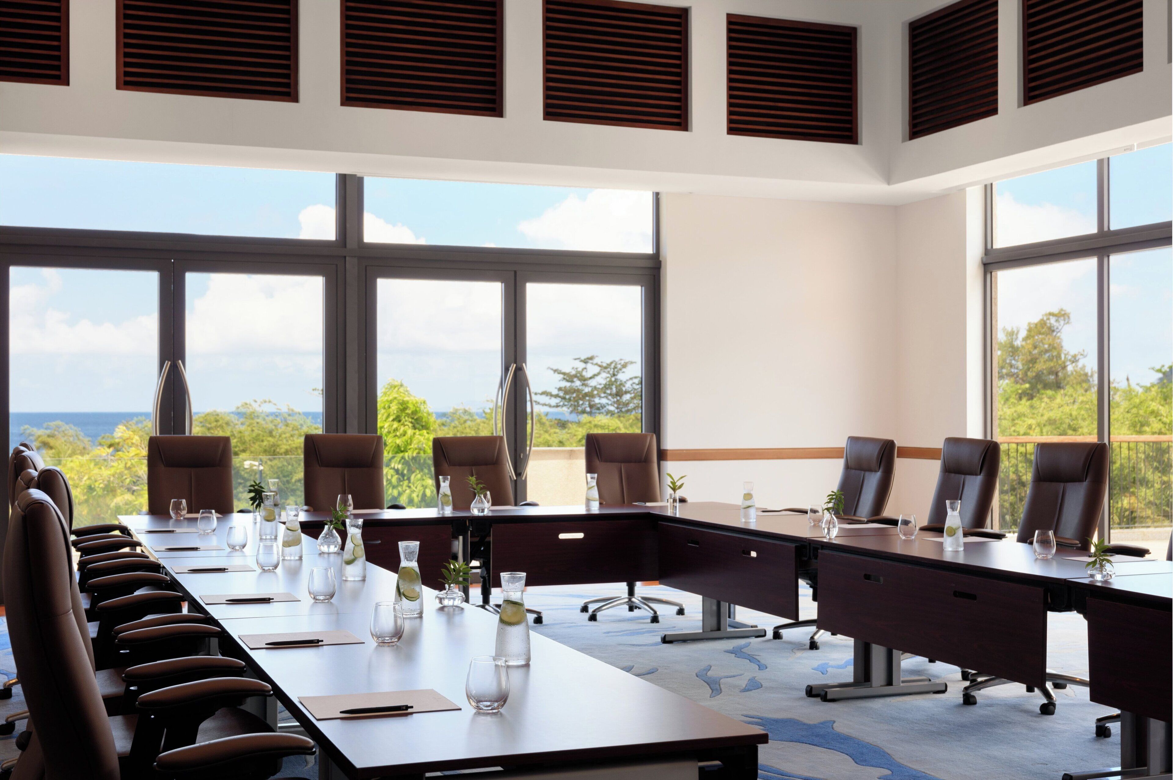 Une salle de conférence dotée d’une longue table, de nombreuses chaises et de grandes fenêtres donnant sur l’extérieur.