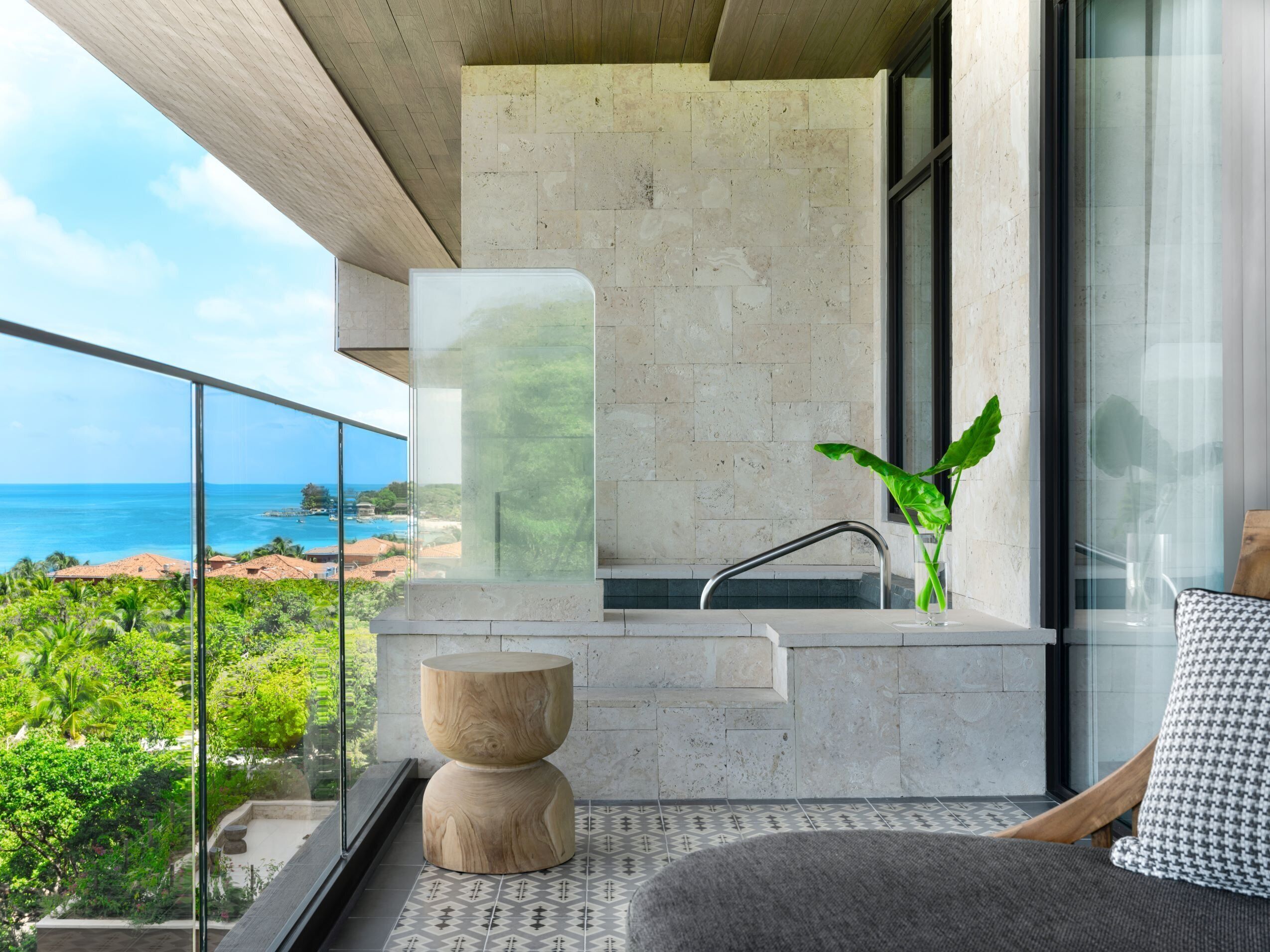 A modern balcony with a view of the ocean, a glass partition, a sink, and a wooden planter.