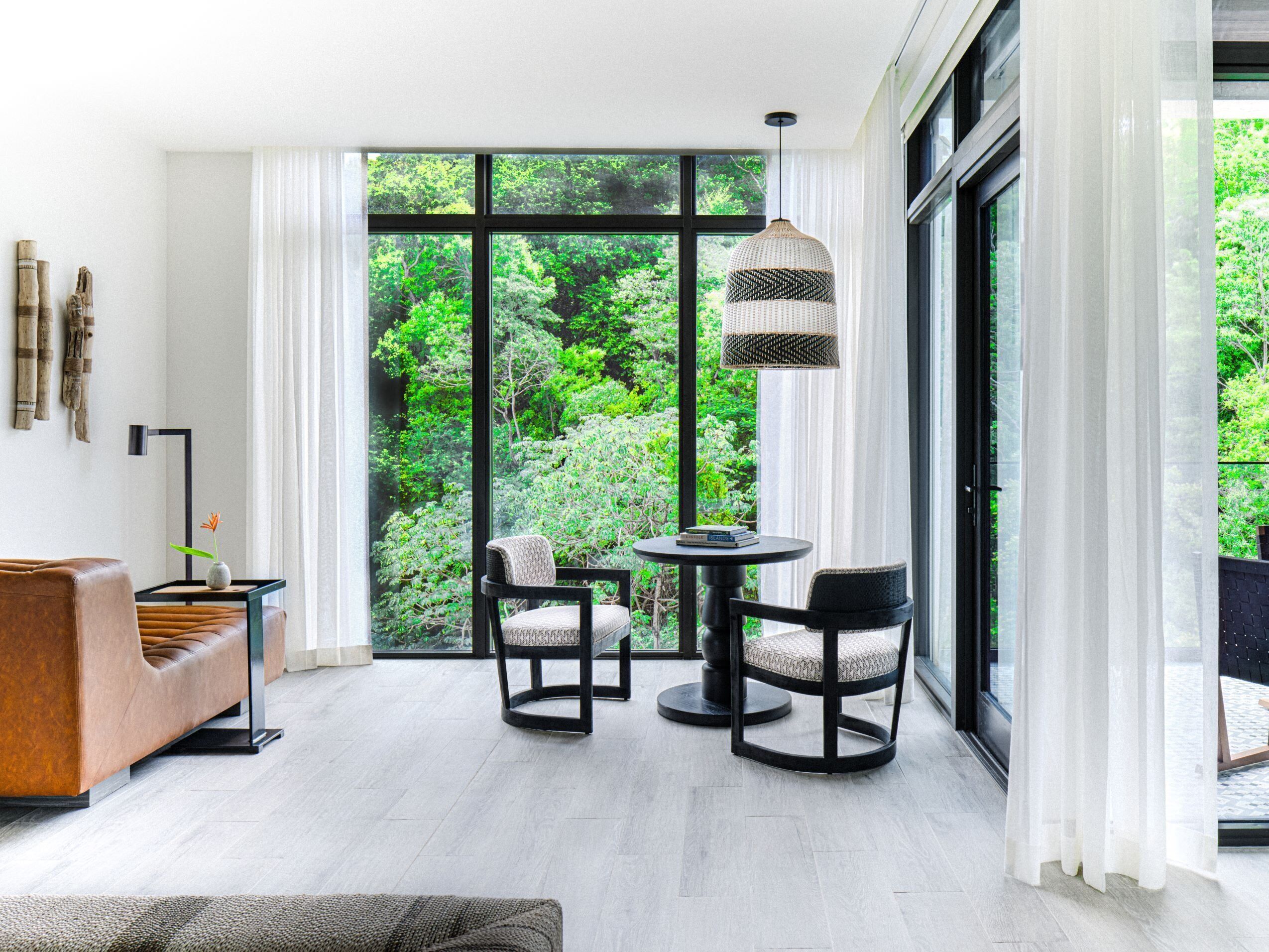 Una sala de estar moderna con un ventanal grande, un sofá, dos sillones, una mesita y un aplique colgante.