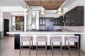 A modern kitchen with a large island, bar stools, and pendant lighting.