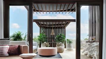 A modern living room with a sofa, ottoman, and coffee table, a wooden pergola, and potted plants.