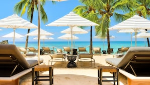 A beachside lounge area with multiple white-striped umbrellas, lounge chairs, and a view of the ocean.