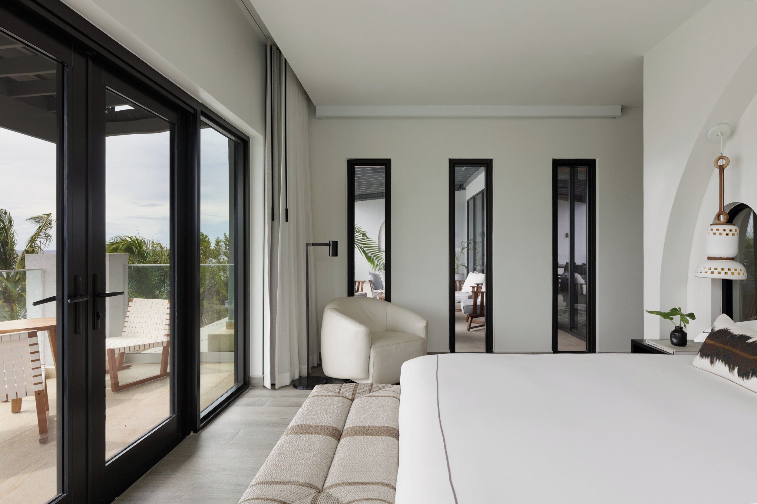 A modern hotel room with a large bed, a seating area, and a balcony with a view.