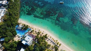 An aerial view of a beach resort with a swimming pool, palm trees, and clear turquoise waters.