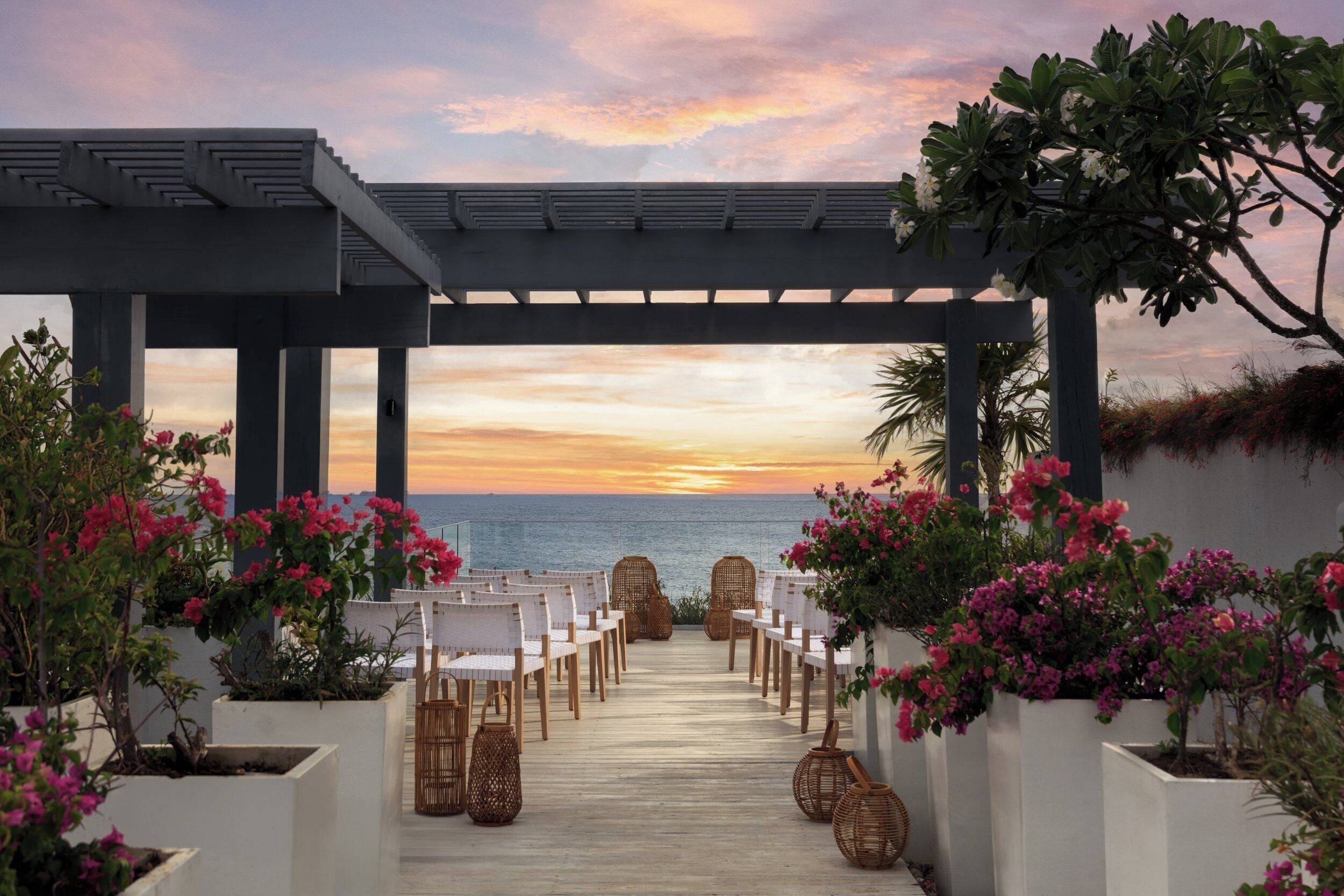 A wooden deck with white chairs arranged for an event, overlooking a body of water at sunset.