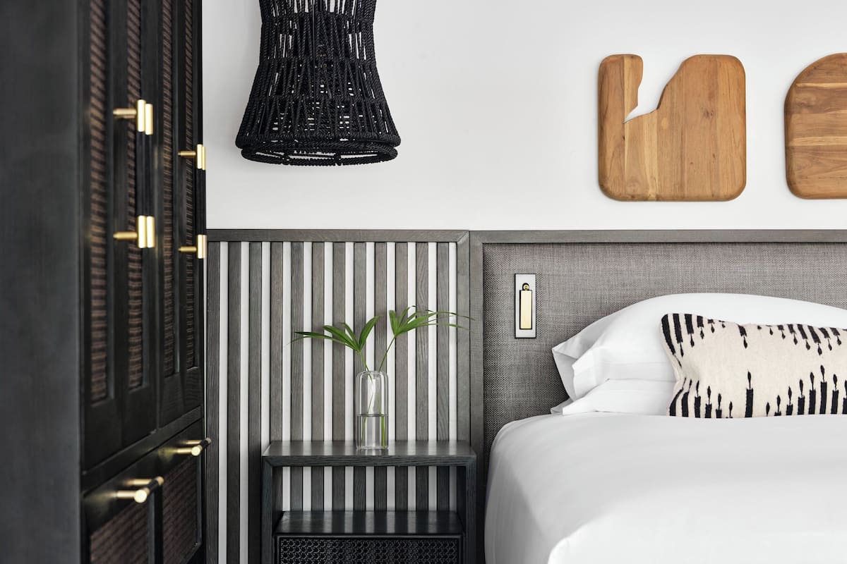 A modern bedroom with a striped headboard, a bedside table with a vase, and a bed with white bedding and patterned pillows.