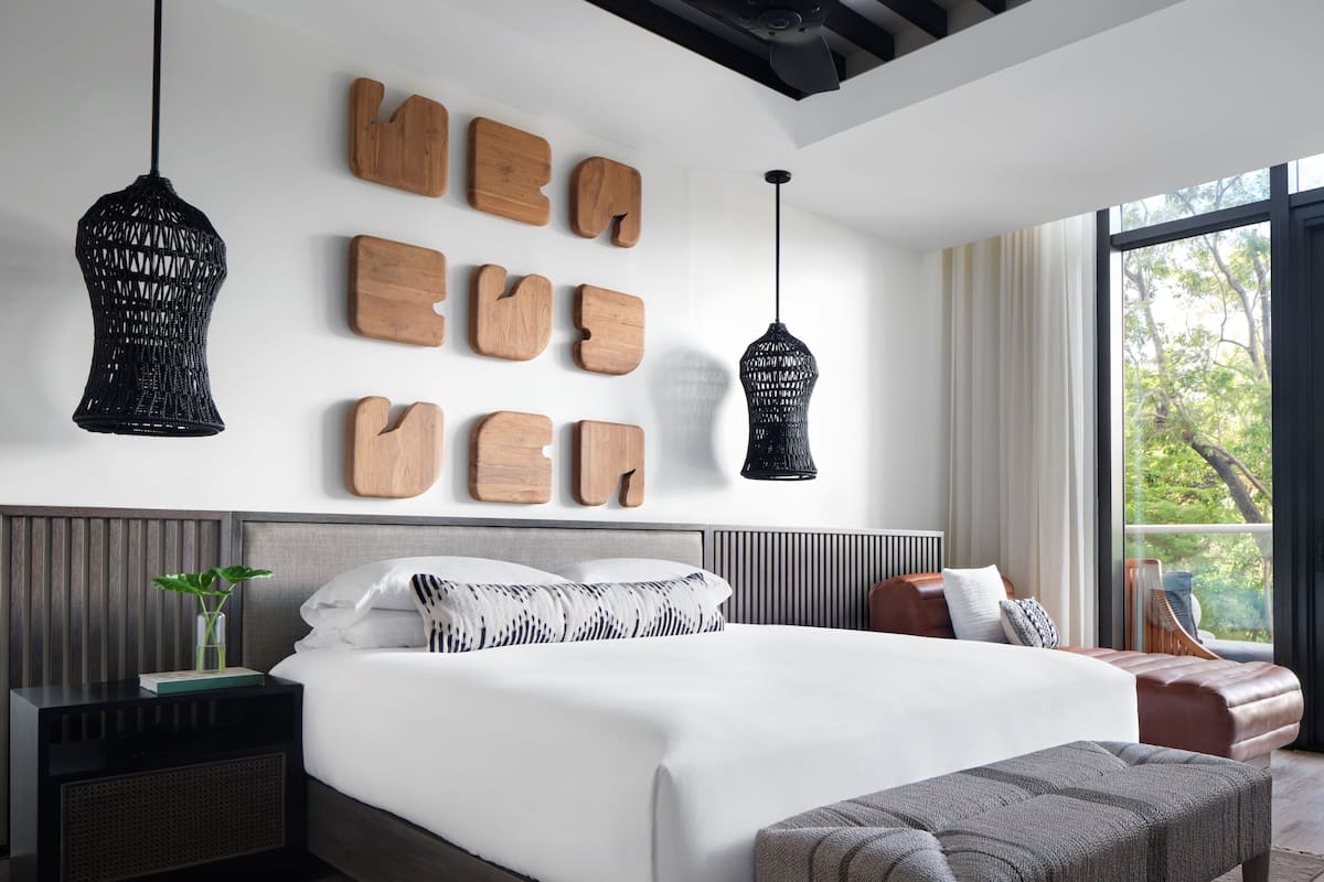 A modern bedroom with a large bed, a bedside table with a plant, a bench, and a wall with wooden letters.