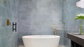 Un baño moderno con una bañera independiente, cabezal de ducha y tocador con planta.