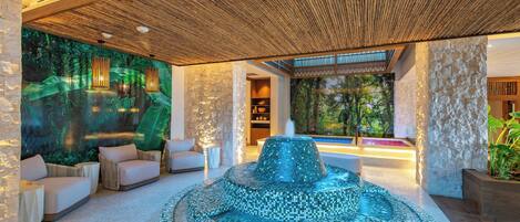 A modern spa area with a mosaic fountain, comfortable seating, and a stone wall backdrop.