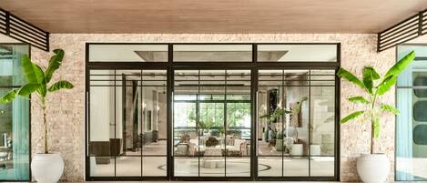 A modern building with large glass doors, brick walls, and potted plants.