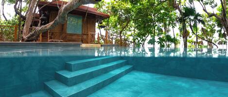 Piscina azul clara con escalones para entrar, rodeada de exuberante follaje y una estructura de madera.