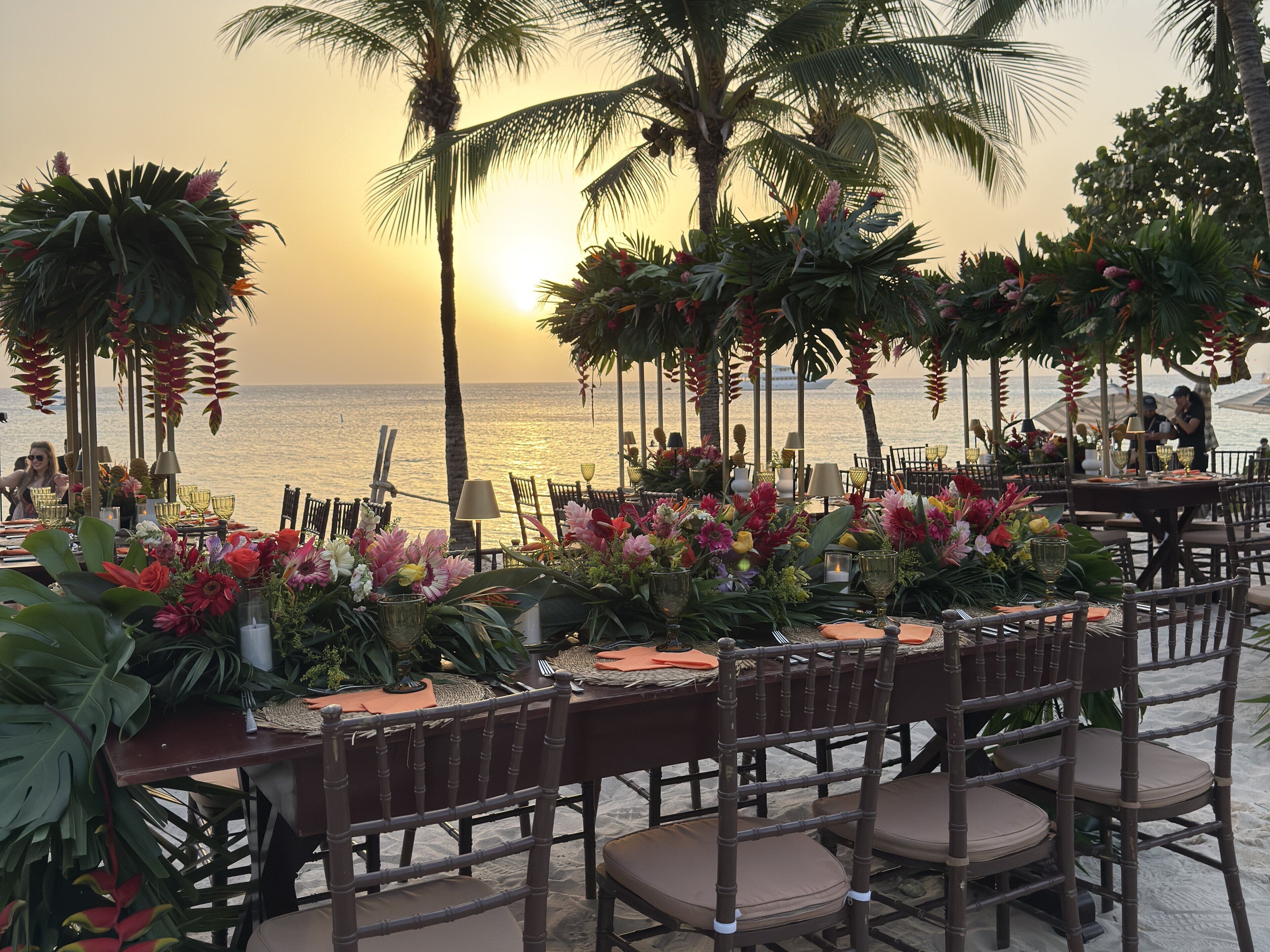 An outdoor dining area with tables set for a meal, overlooking the ocean at sunset.