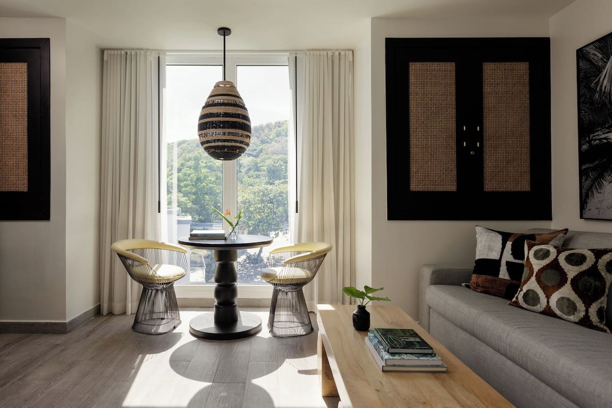 A modern living room with a round table, two chairs, a sofa, and a hanging light fixture.