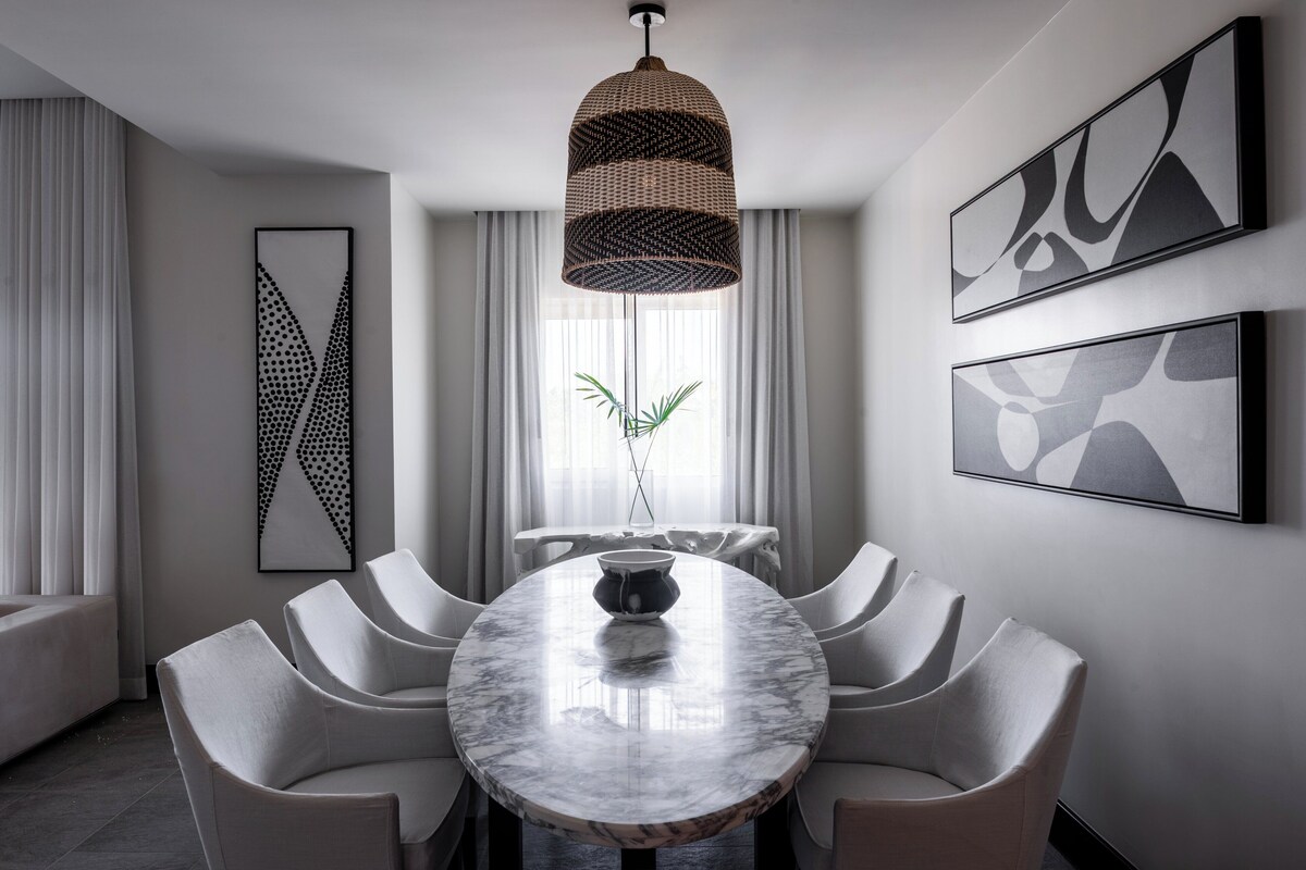 A modern dining area with a marble table, white chairs, a hanging pendant light, and abstract wall art.