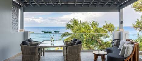 A covered outdoor seating area with wicker furniture and a view of the ocean.