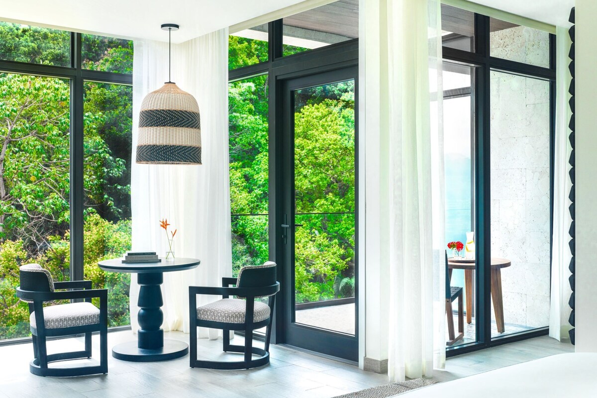 A modern room with large windows, a round table, two chairs, and a hanging light fixture.