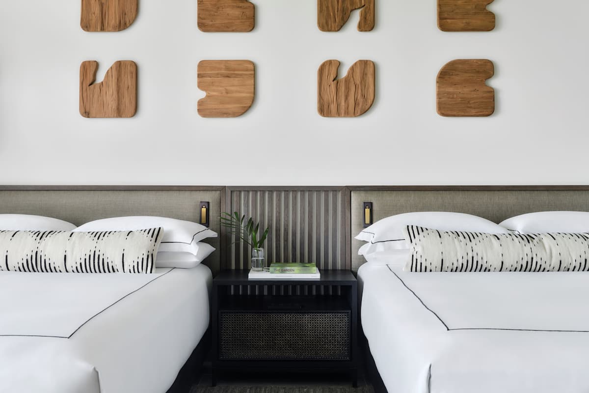 A modern hotel room with two beds, a nightstand, and a wall-mounted wooden art piece.