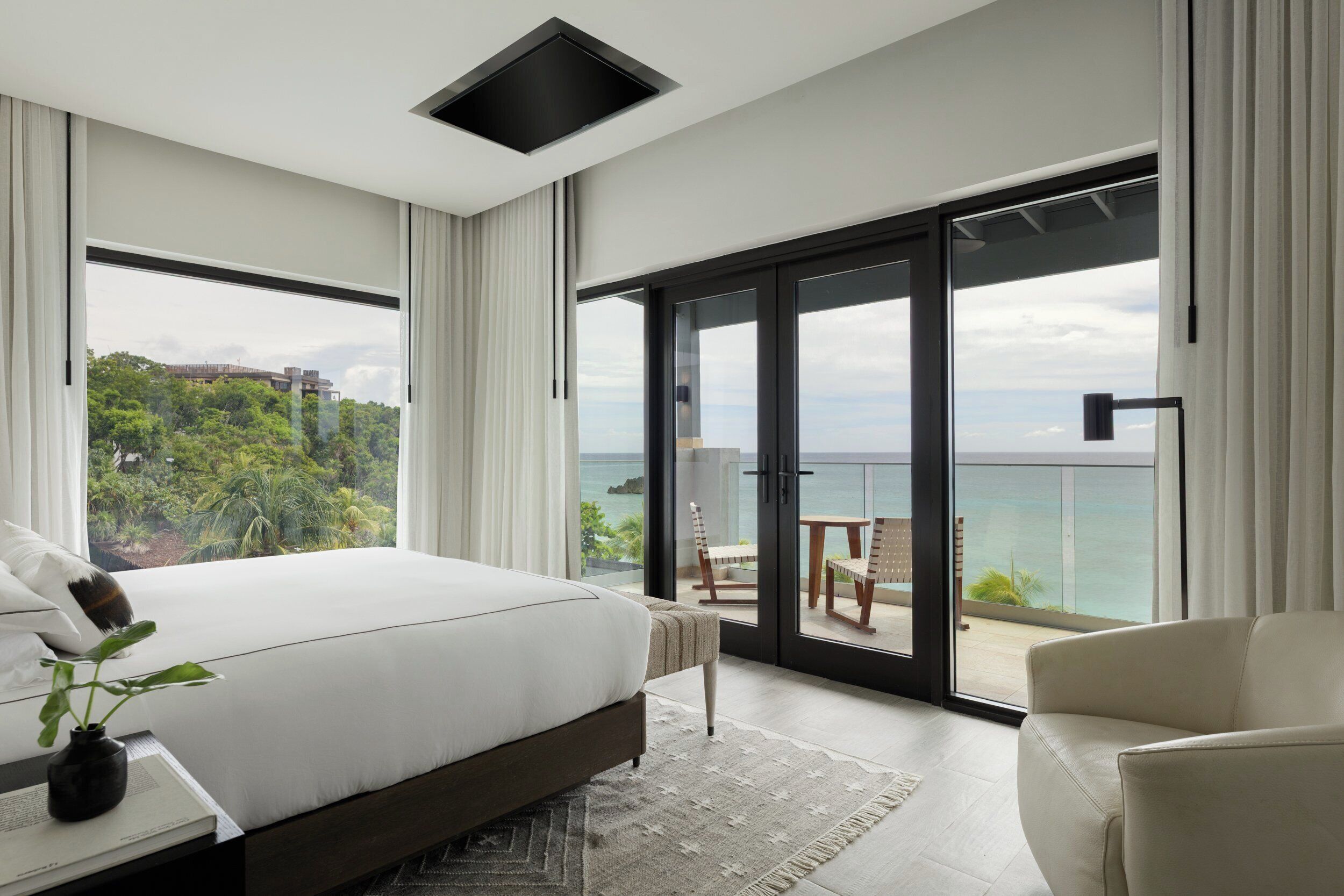Een moderne slaapkamer met een groot bed, uitzicht op zee en een balkon met zitplaatsen.