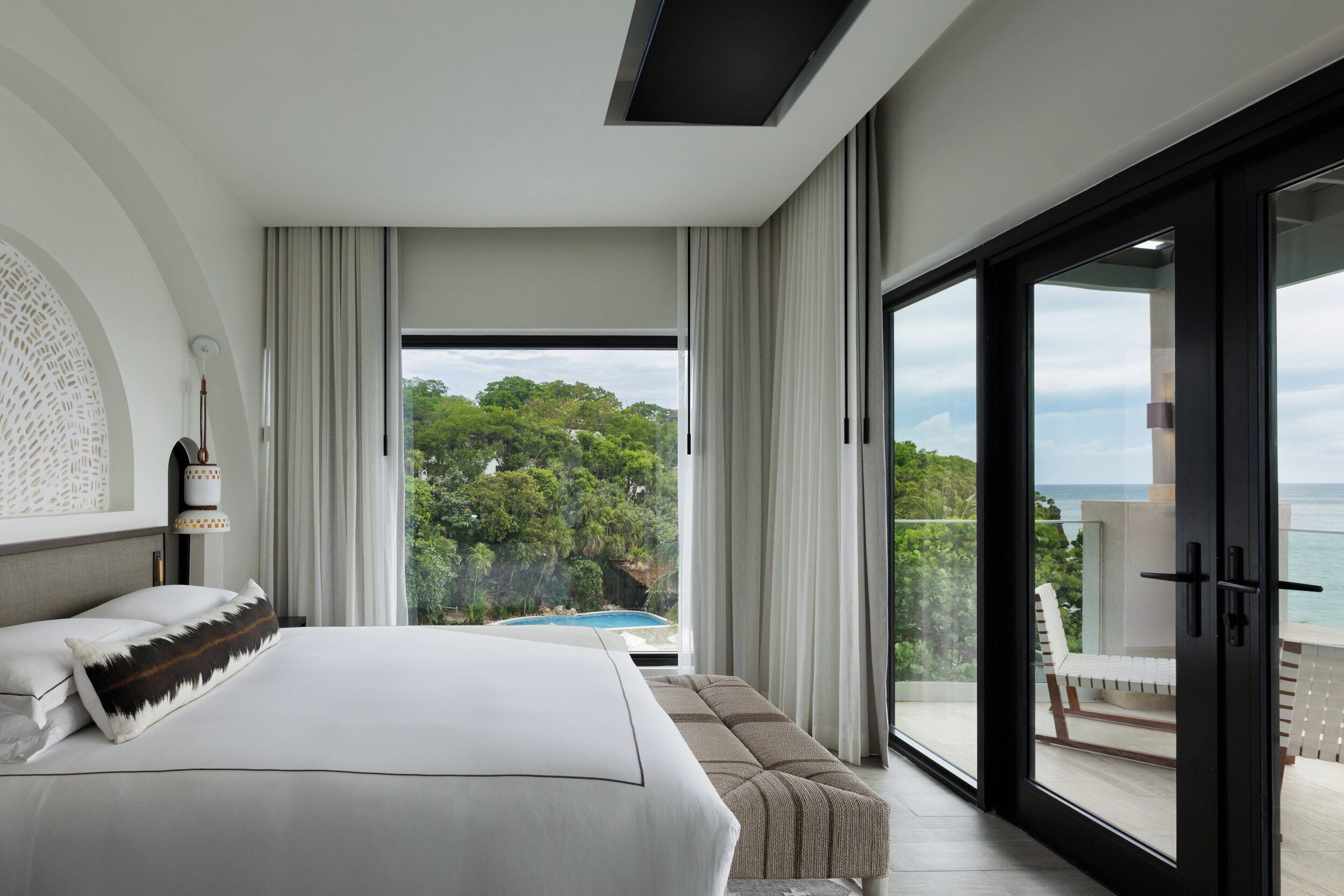A modern hotel room with a large bed, a sofa, and a balcony with a view of the sea.