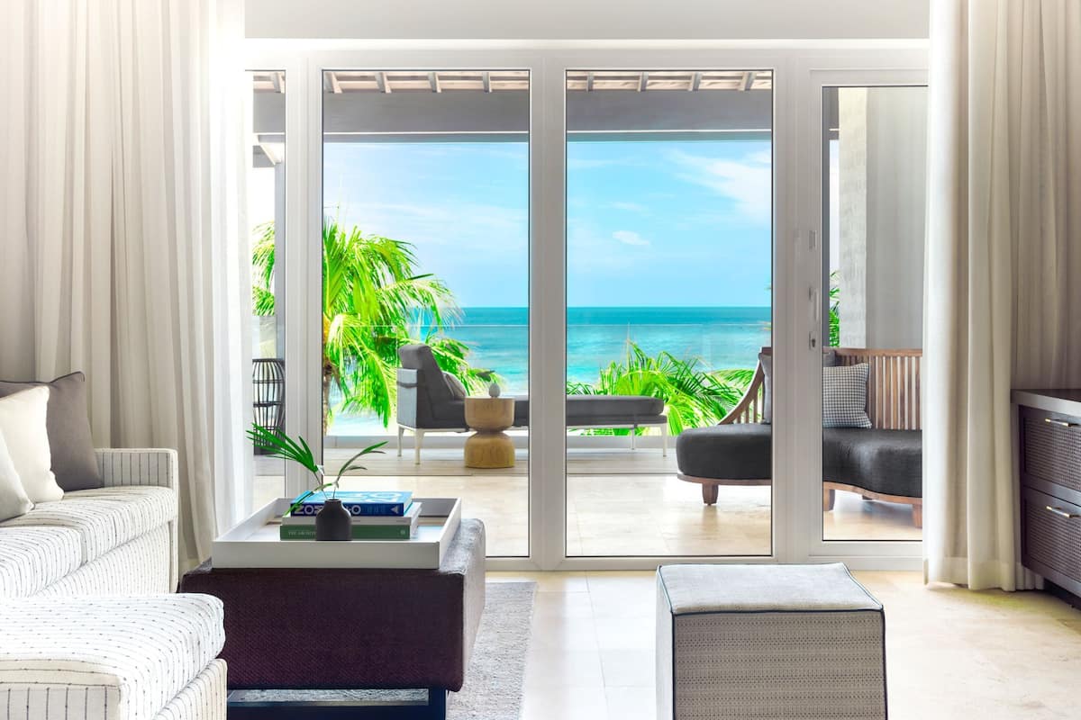 A modern living room with a large sliding glass door leading to a balcony with a view of the ocean.