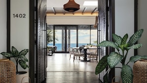 A modern hotel lobby with a dining area, large windows, and tropical plants.