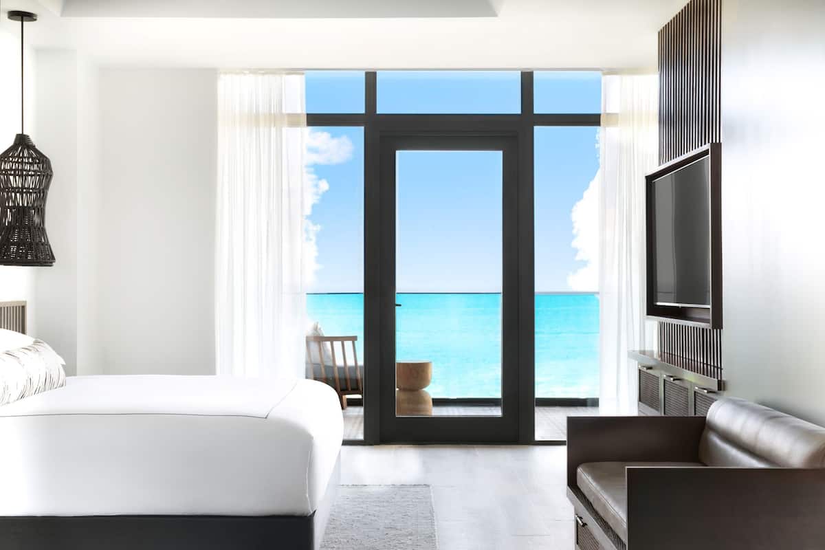 A modern hotel room with a large bed, a TV, and a view of the ocean.