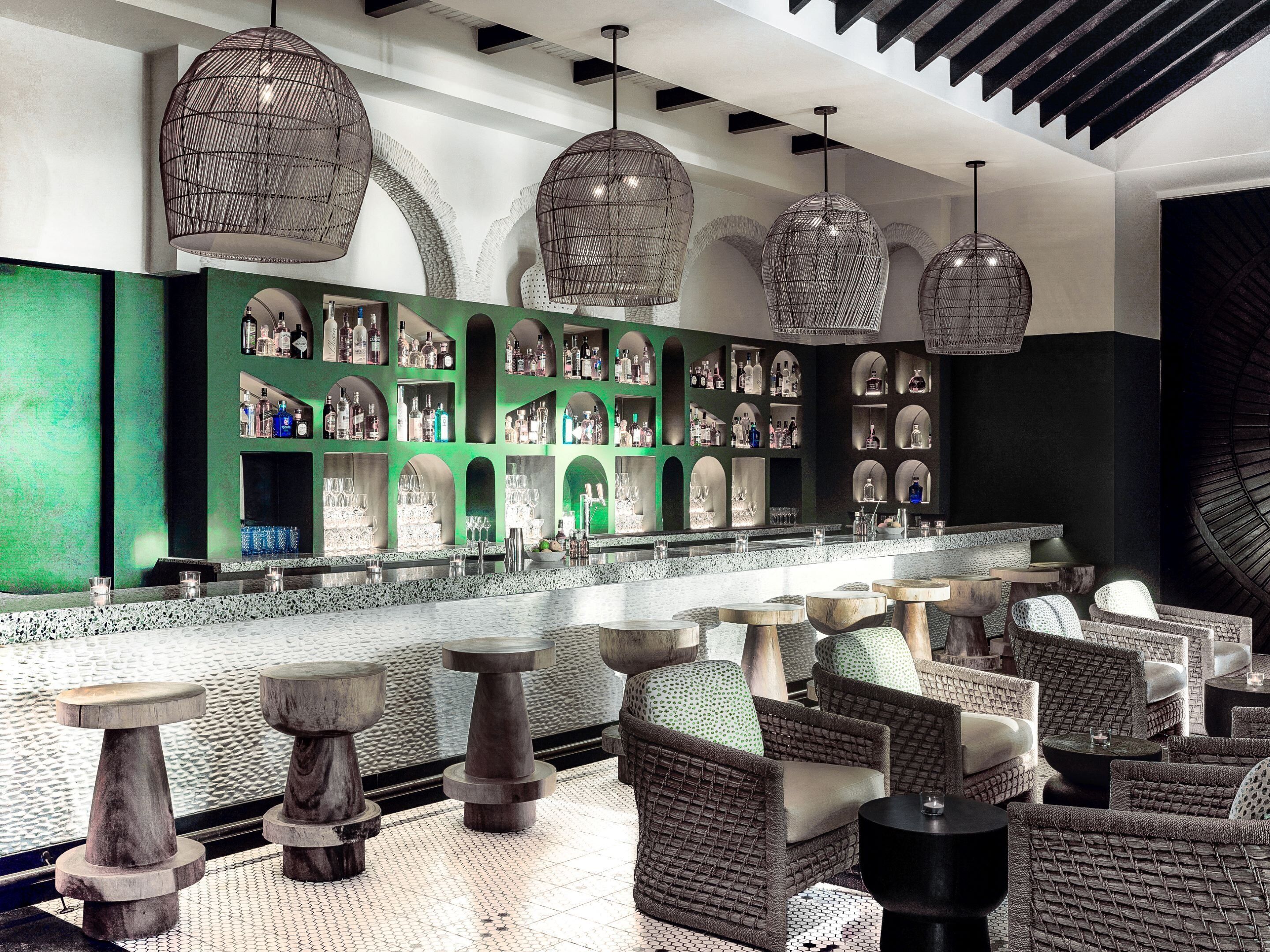 A bar area with multiple seating options, including chairs and stools, and a variety of bottles and glasses on shelves.