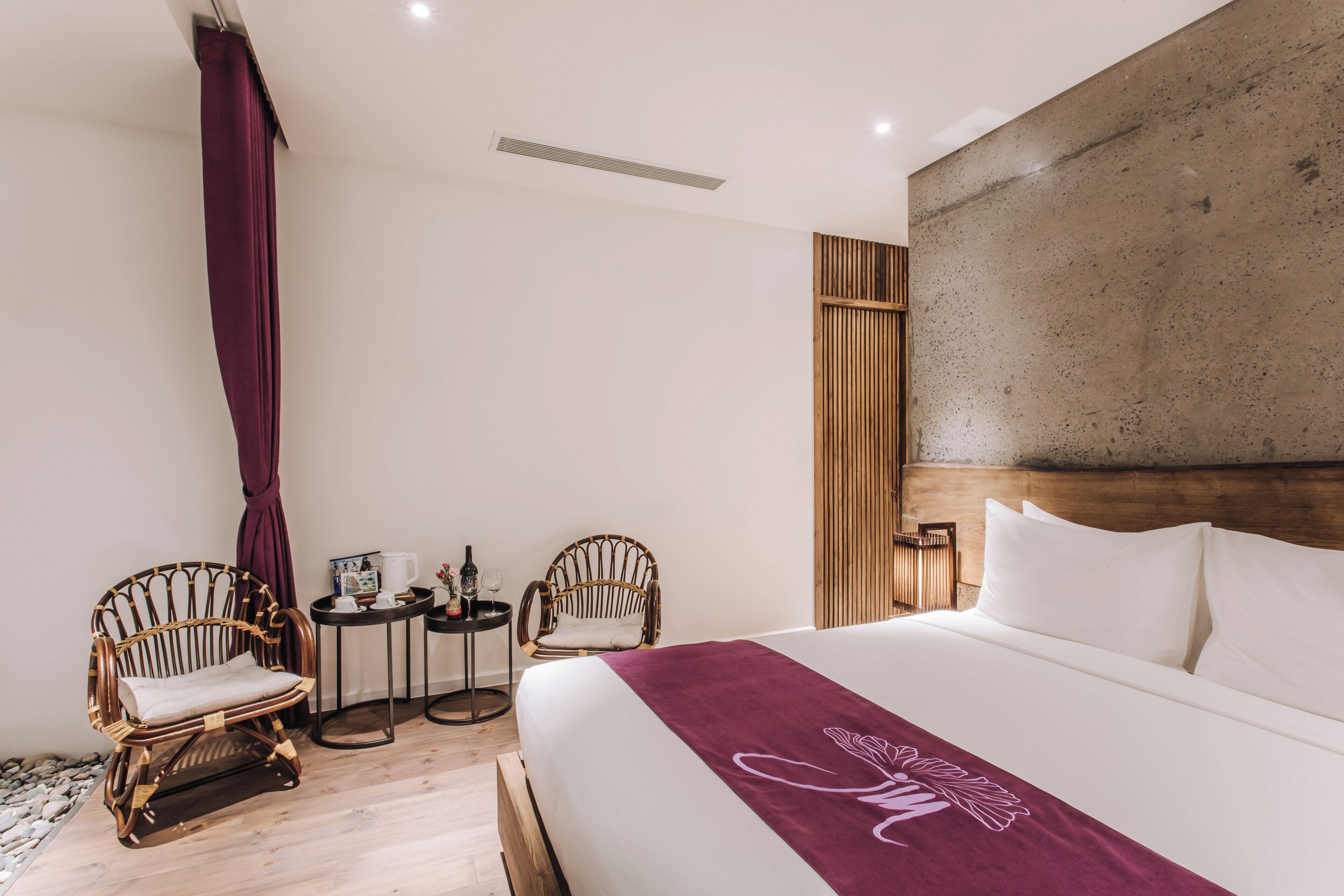 A hotel room with a large bed, two wicker chairs, a small round table with a coffee pot, and a wooden headboard.