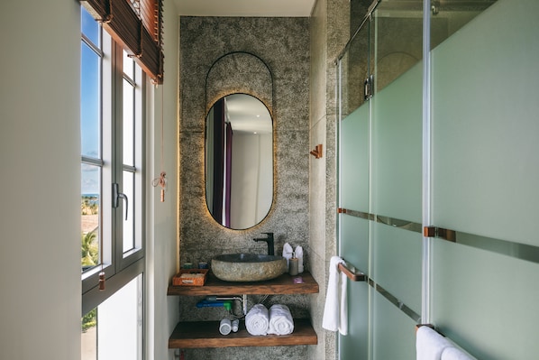 A bathroom with a stone sink, a large mirror, and a glass shower enclosure. - JM Boutique Hotel (Phu Quoc)
