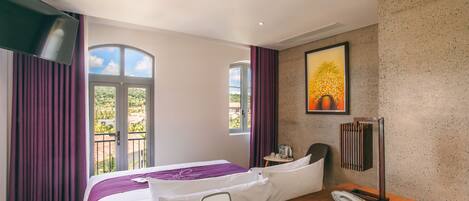 A hotel room with a bed, a desk with a telephone, and a window with curtains.