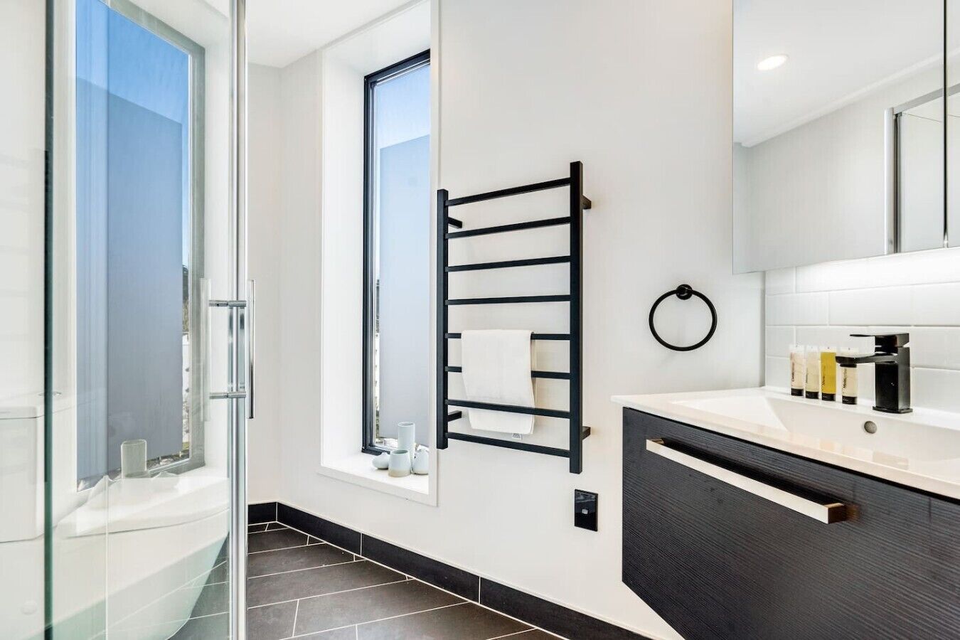 A modern bathroom with a glass shower, a black towel rack, a white sink with a black faucet, and a large mirror.