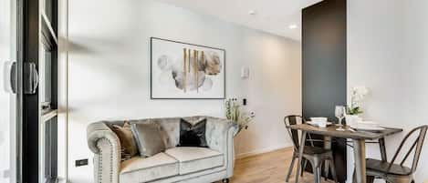 A modern living room with a sofa, dining table, chairs, and a framed artwork on the wall.